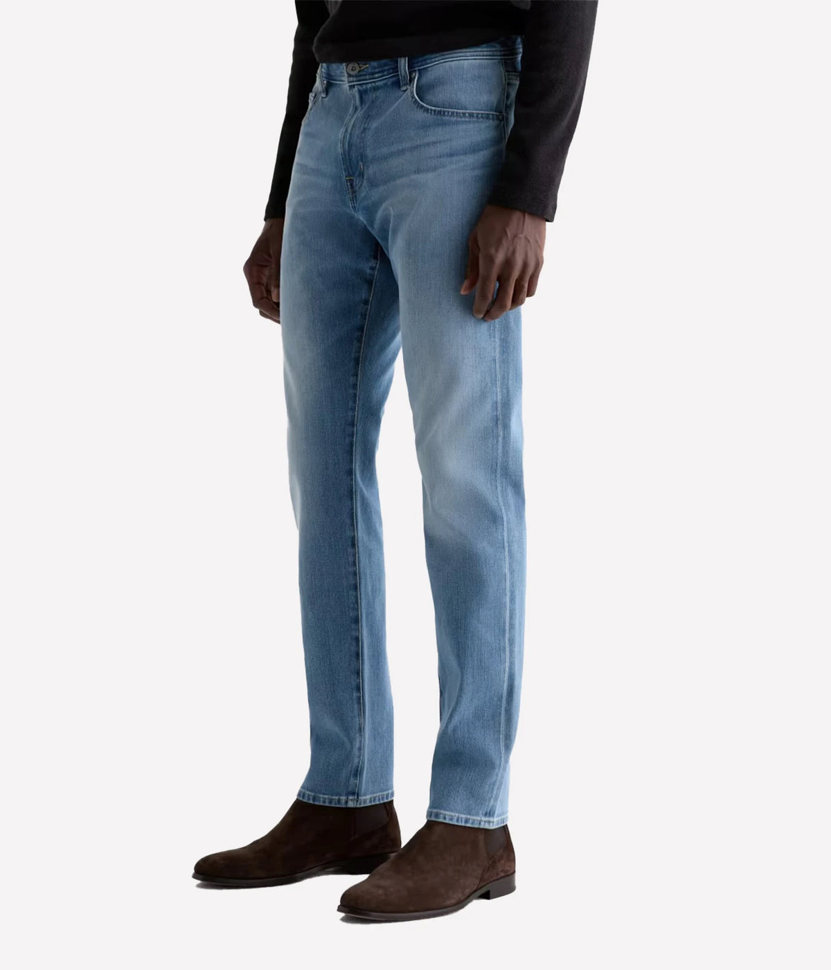 A person wearing light blue slim-fit jeans, a black long-sleeve top, and dark brown suede boots, shown from the waist down against a plain light gray studio background.