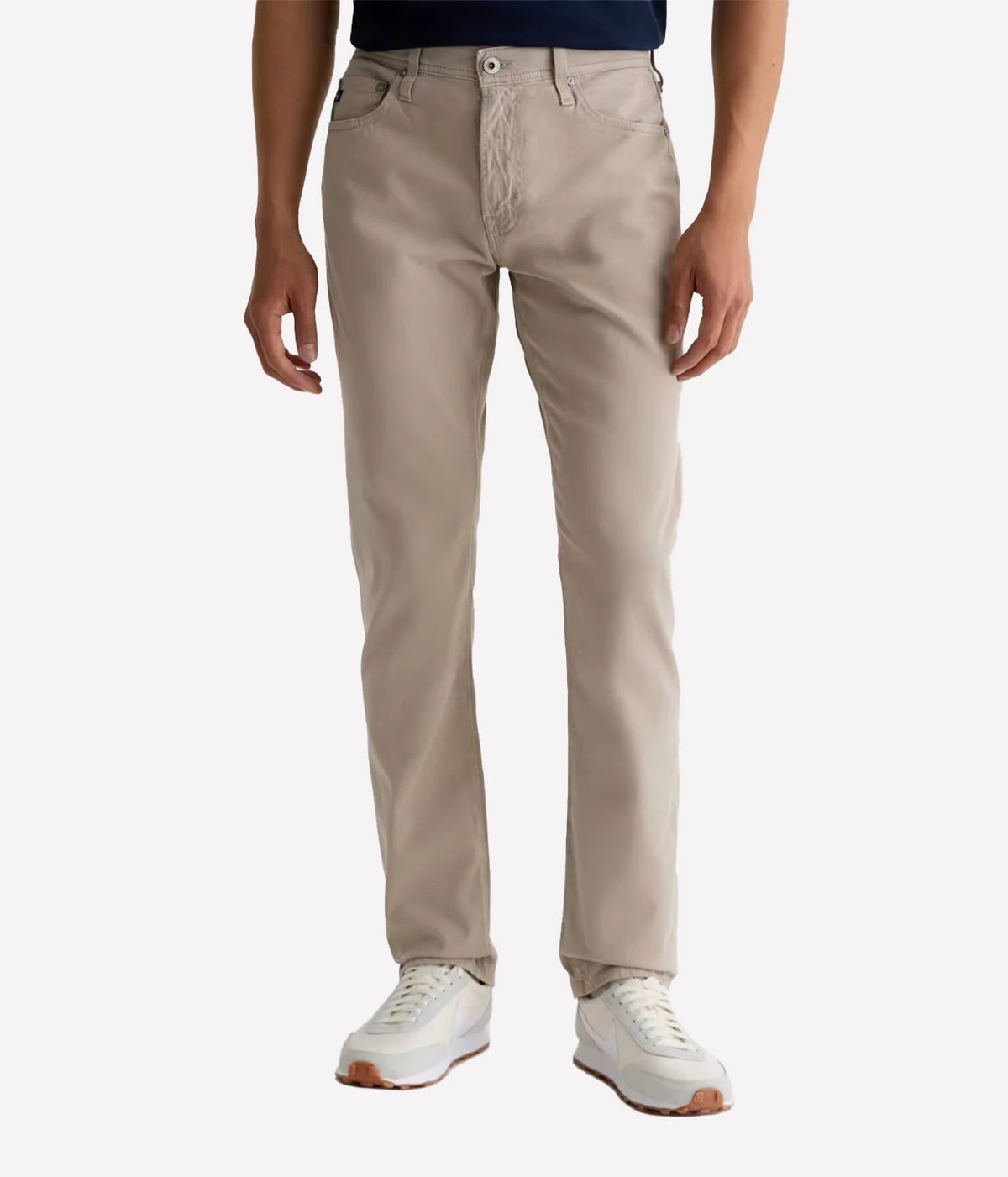Man wearing AG Everett SUD Pant in Desert Stone with a navy tee and white sneakers, front view
