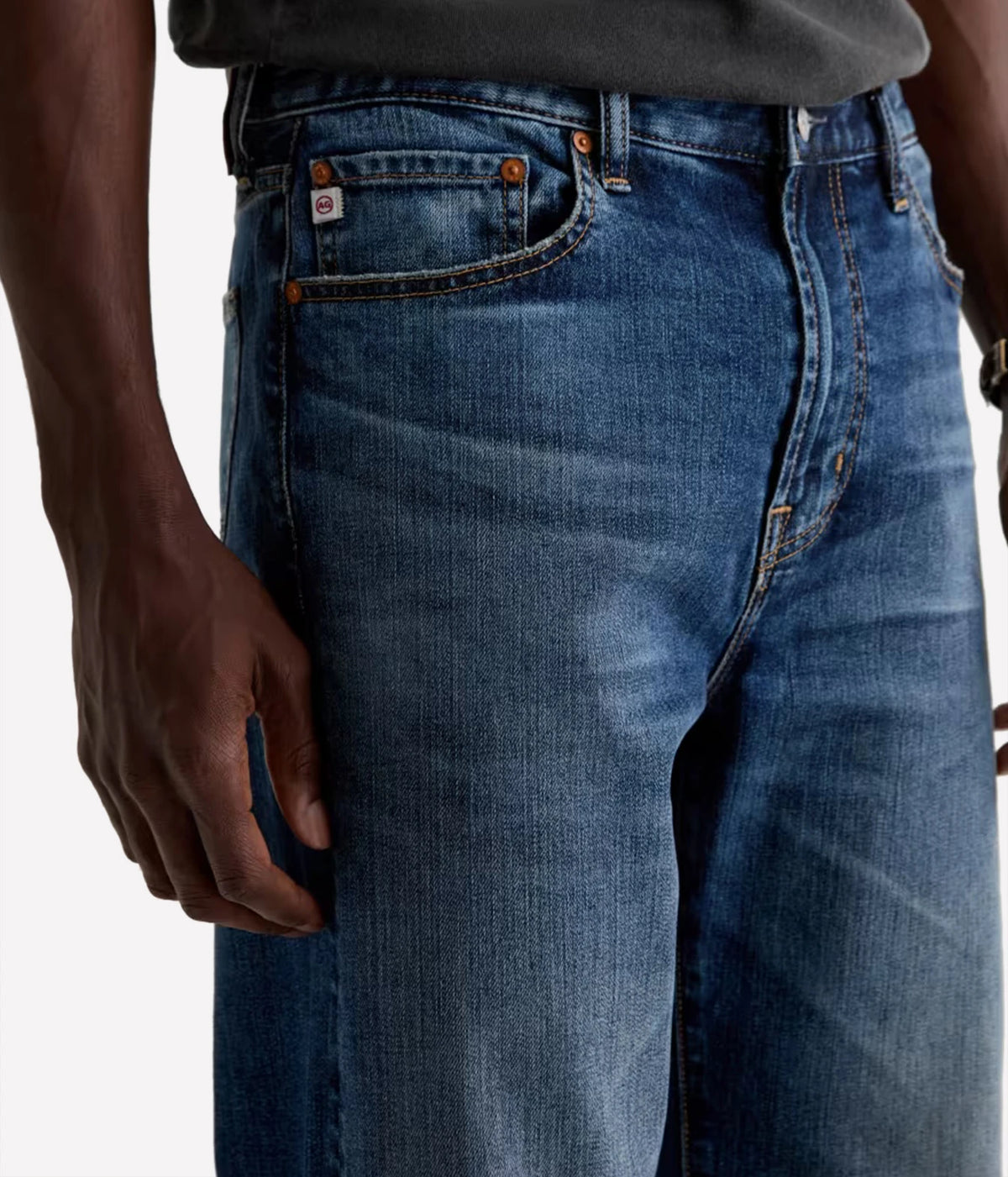 Close-up of a person wearing blue denim jeans with a faded wash, showing the front pocket, belt loops, and waistband against a plain light background.