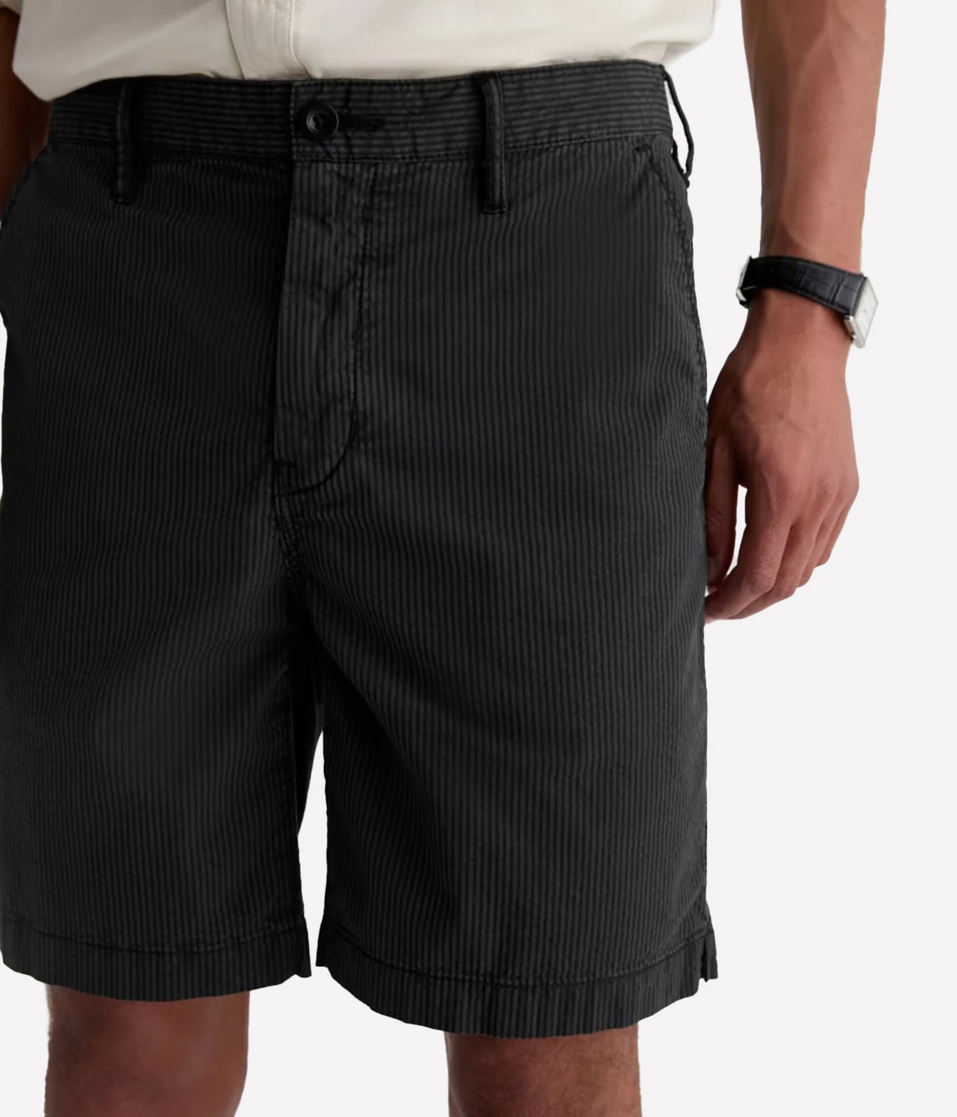 Close-up of a person wearing dark charcoal pinstriped shorts with a white shirt and a black watch, shown against a plain light background.