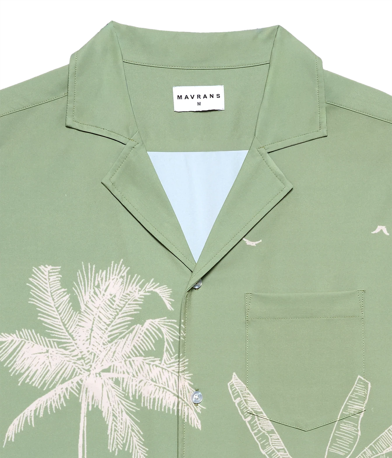 A close-up of a sage green short-sleeve camp collar shirt by Mavrans, featuring a white palm tree print on the front, a white inner collar lining, and a white brand label.