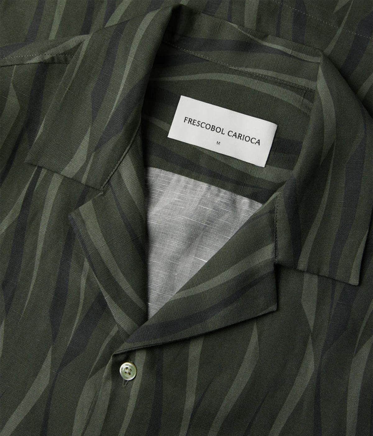 Close-up of a Frescobol Carioca Roberto Short Sleeve Linen-Blend Shirt in Cove Green, featuring a dark olive green and black wavy stripe pattern with a white brand label visible inside the collar.