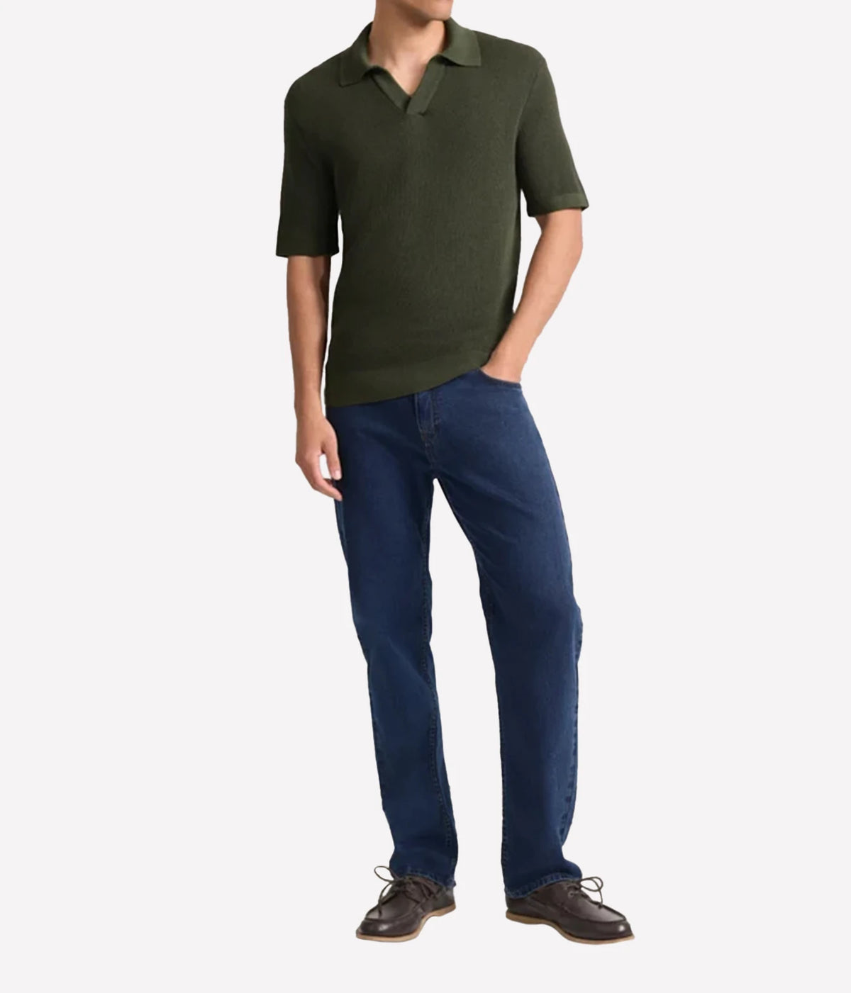 A man wearing a Frescobol Carioca Rino Short Sleeve Cotton Polo in Cove Green, dark blue jeans, and brown leather shoes, standing against a light grey background.