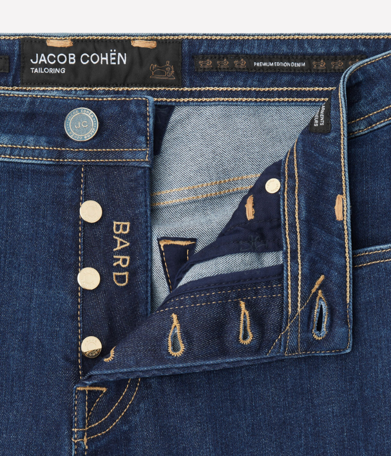 Jacob Cohën's Bard 5 Pocket Jeans from the exclusive Black Label Diamond Edition, crafted from dark blue super-stretch denim with a soft enzyme-washed finish. Features include subtle abrasions, logo embroidery on the coin pocket, a removable black calf hair patch with a gold-tone logo and diamond dust JC motif, and a light gold-tone button with cobalt-blue enamelled edges and diamond dust.