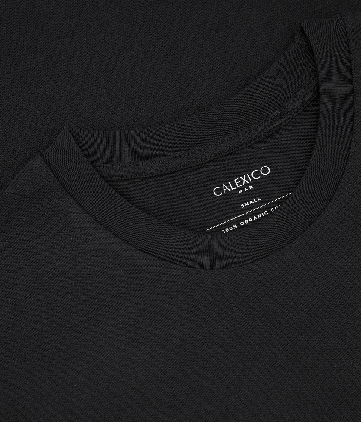 Close-up of a black crewneck t-shirt showing the inner neck label with white text that reads 'CALEXICO SMALL 100% ORGANIC CO'.