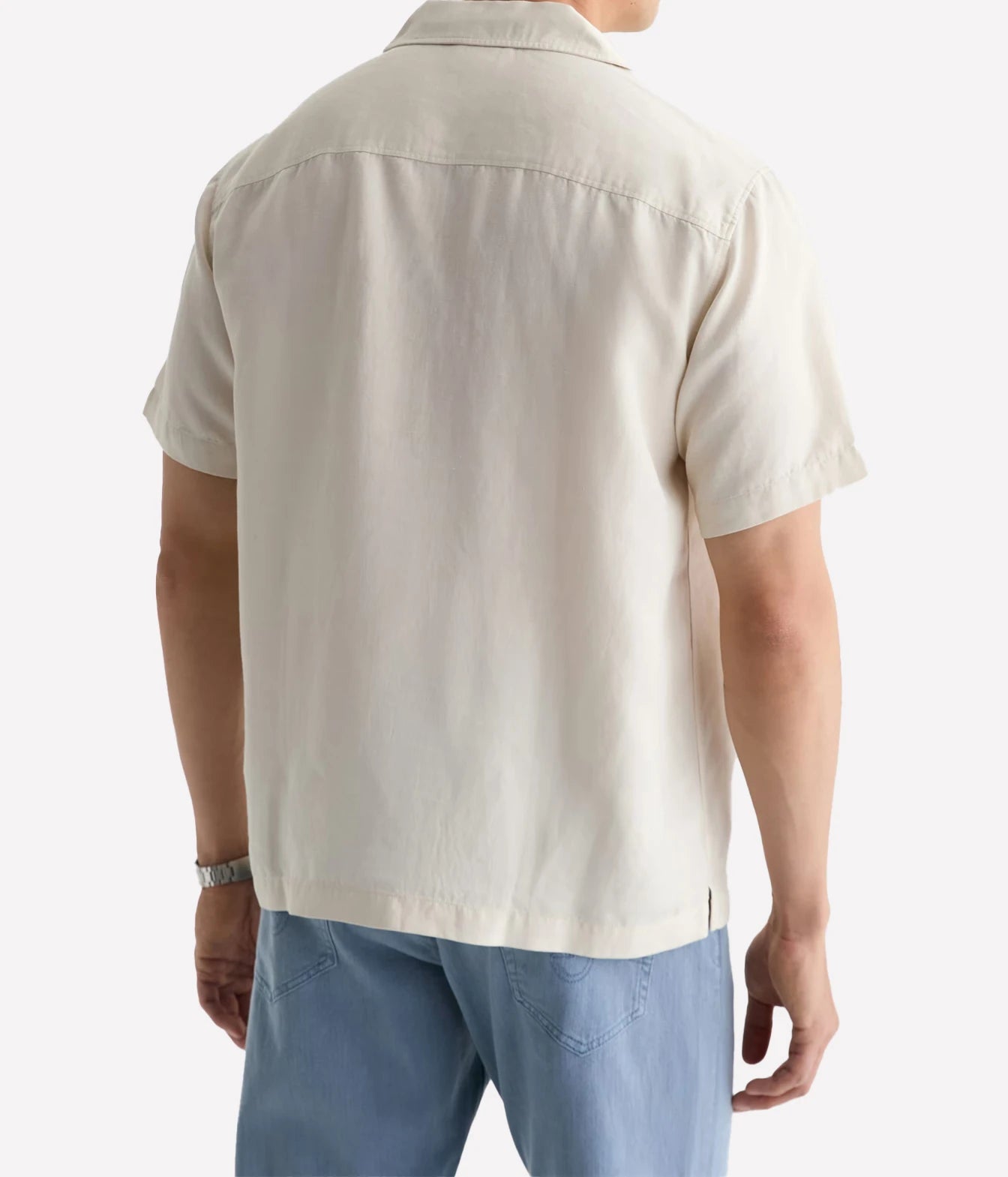 A man wearing a short-sleeve cream-colored camp collar shirt, shown from the back, paired with light blue jeans against a plain white background.