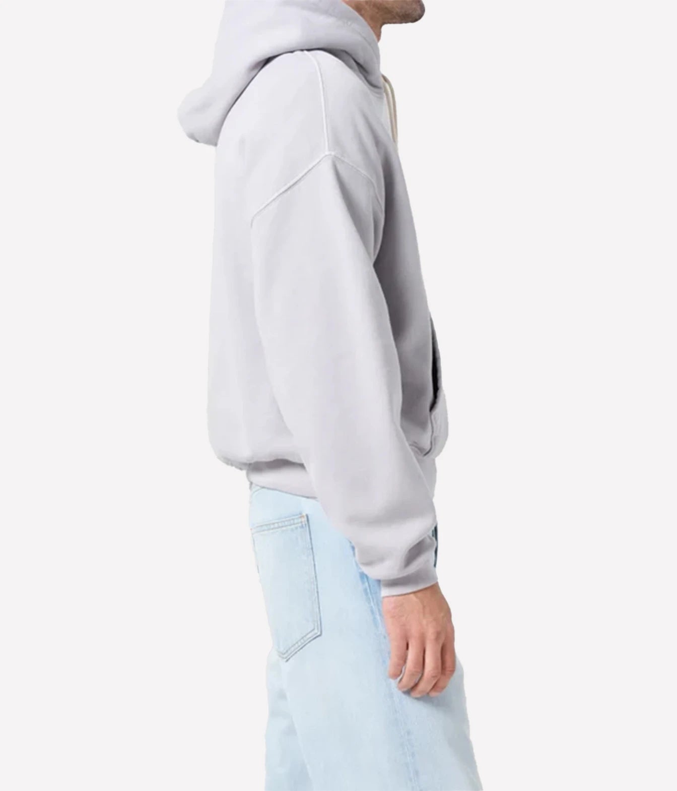 A side profile view of a person wearing a light gray oversized pullover hoodie and light blue jeans against a plain white background.