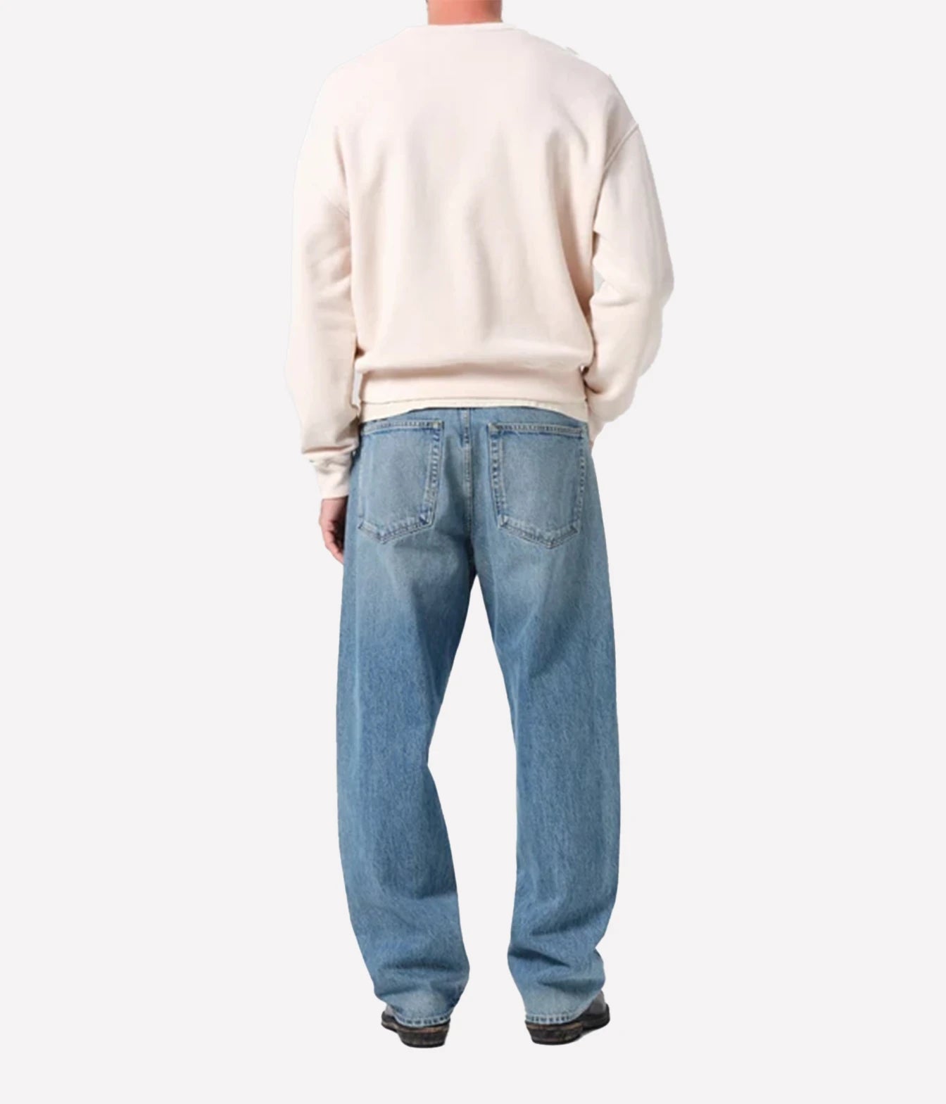 A person shown from the back wearing a cream sweatshirt and light blue relaxed-fit jeans, photographed against a plain light gray studio background.