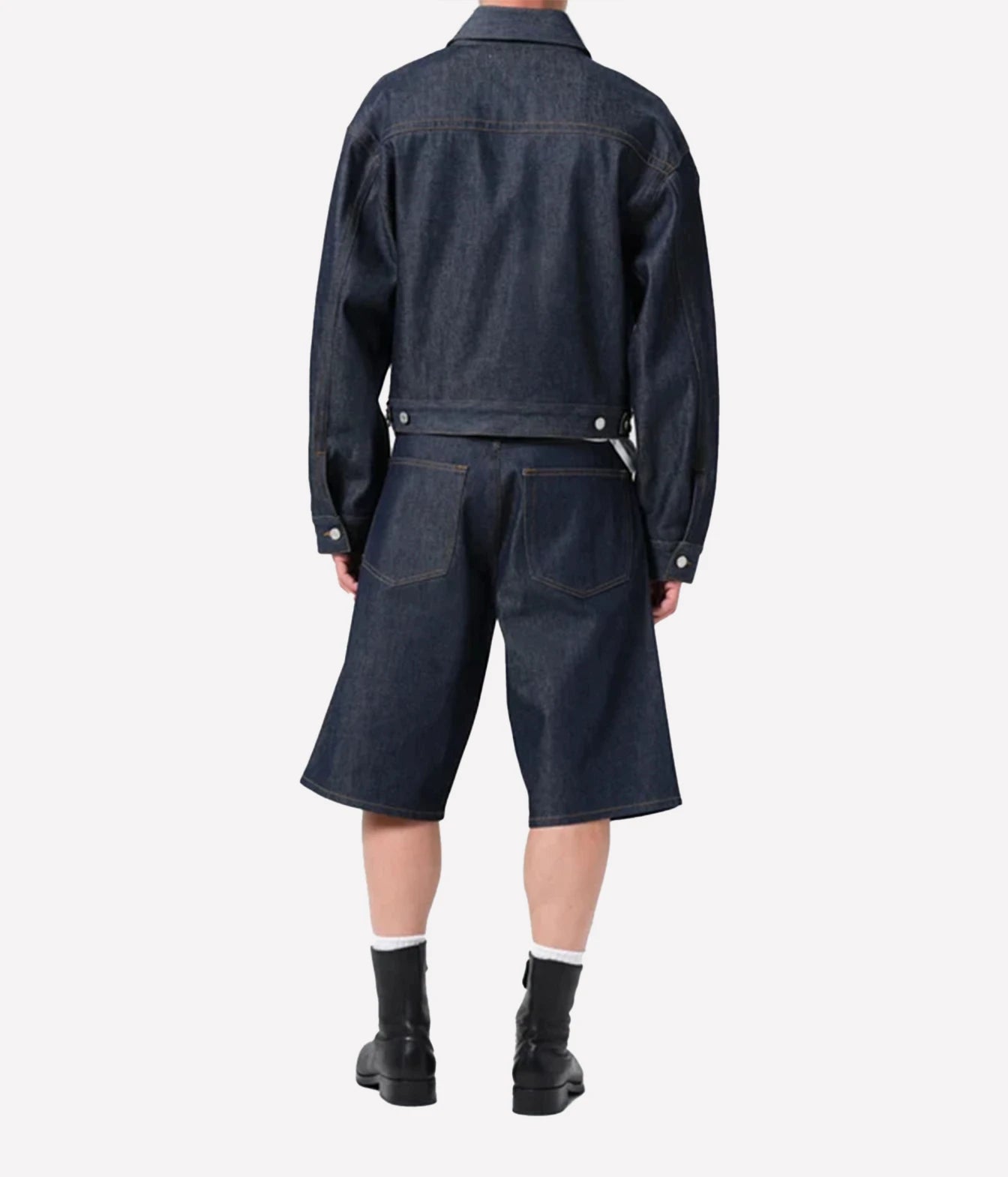 A model shown from the back wearing a dark indigo denim jacket and matching cropped denim shorts, paired with black boots and white socks, against a plain light gray background.