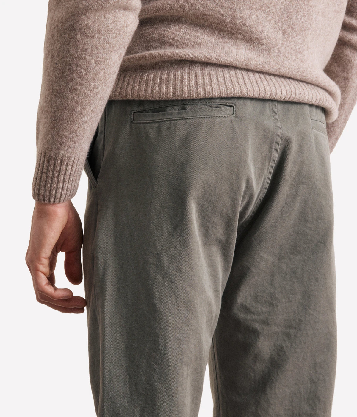 Close-up back view of a person wearing a ribbed knit sweater and olive green trousers against a plain light background.