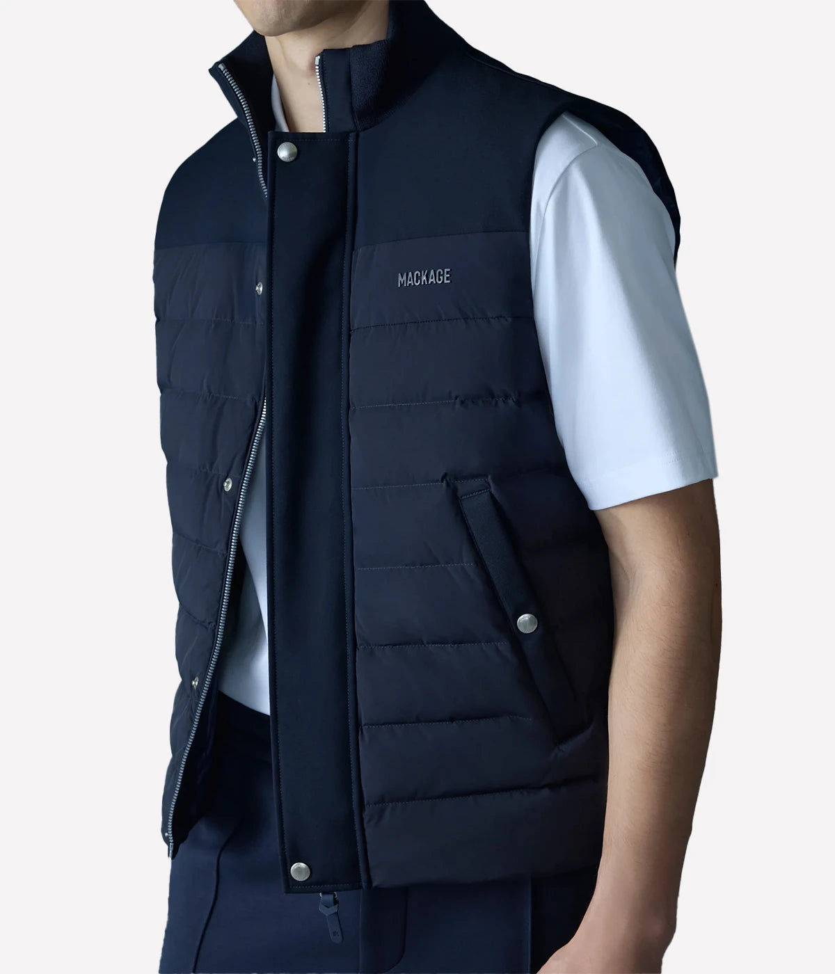 Quilted down vest with stretch nylon and twill panels, ribbed collar, and snap-secured pockets, designed for lightweight warmth and layering.