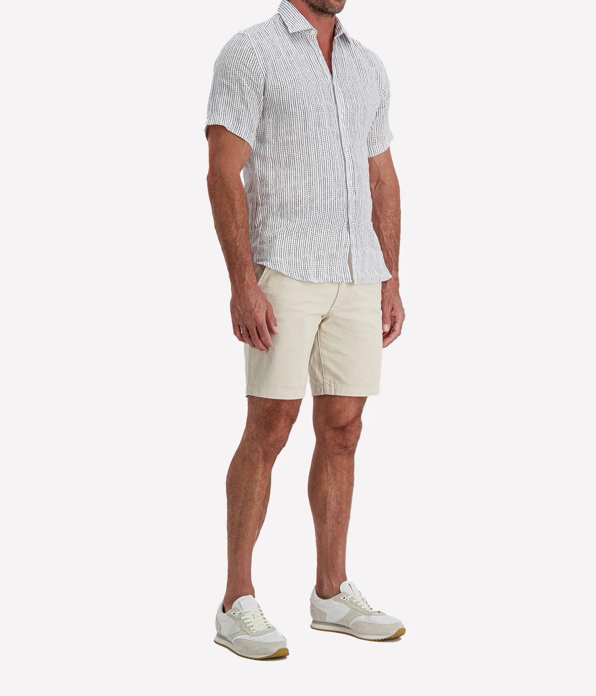 Man wearing Osvaldo Trucchi Linen Short Sleeve Shirt in Navy Woven Stripe with stone shorts and white sneakers, side view