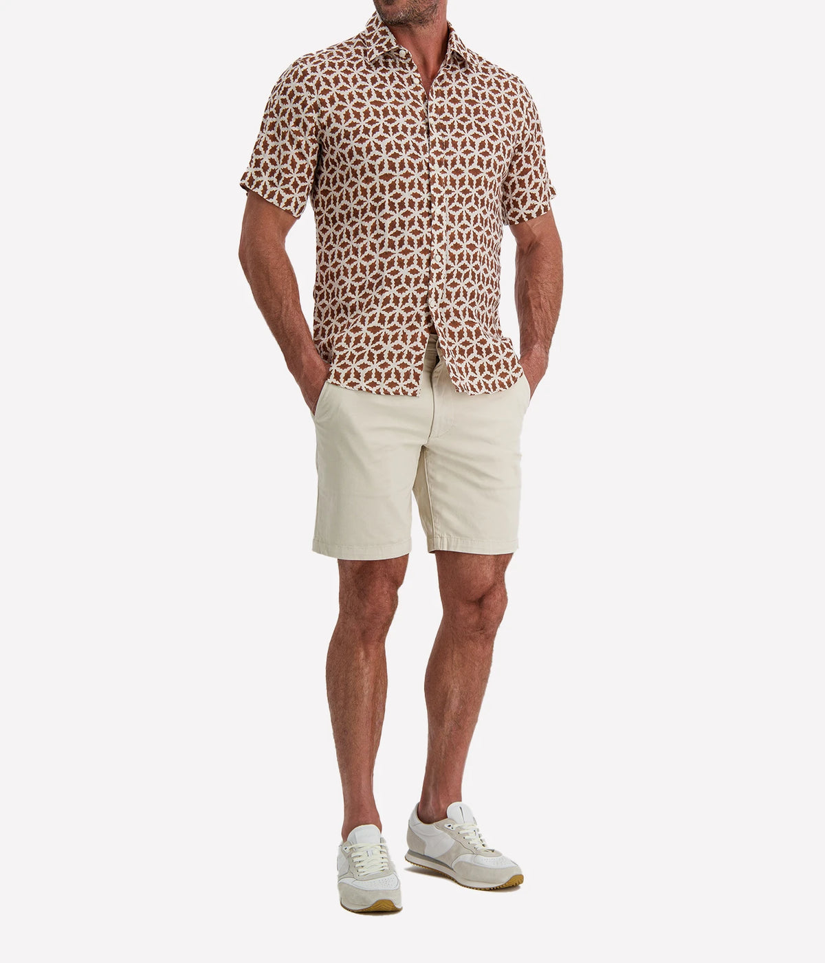 Man wearing Osvaldo Trucchi Linen Short Sleeve Shirt in Brown Geo Star Print with stone shorts and white sneakers, front view with hand in pocket