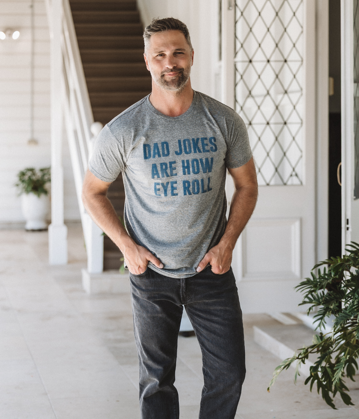 Man wearing a gray t-shirt with 'Dad jokes are how eye roll' text in a home setting.