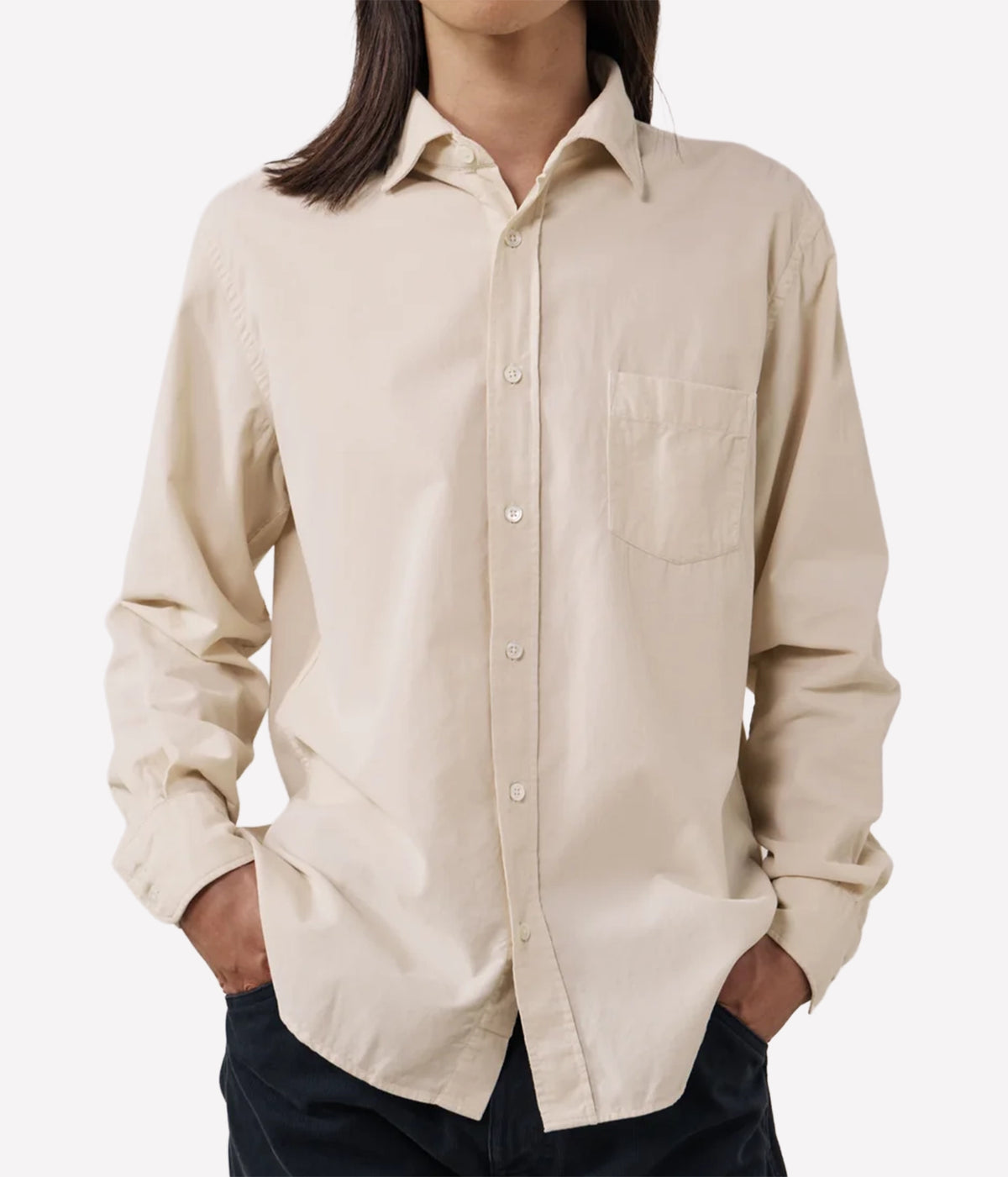 A man wearing a light beige long-sleeve button-up shirt with a chest pocket, paired with dark pants, shown against a plain light grey background.