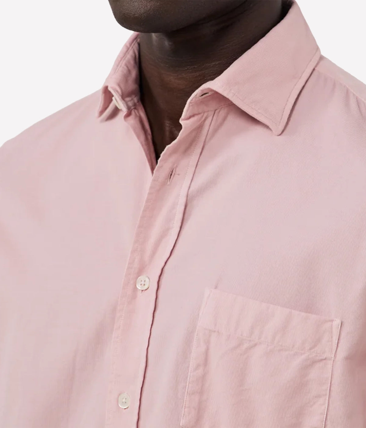 Close-up of a man wearing a light pink button-down shirt, showing the collar, chest pocket, and front buttons against a plain light background.
