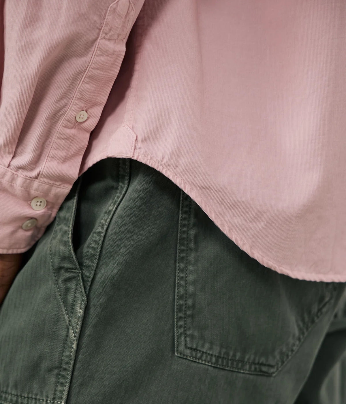Close-up of a person wearing a dusty pink button-up shirt and dark olive green pants, focusing on the fabric texture and pocket detail.