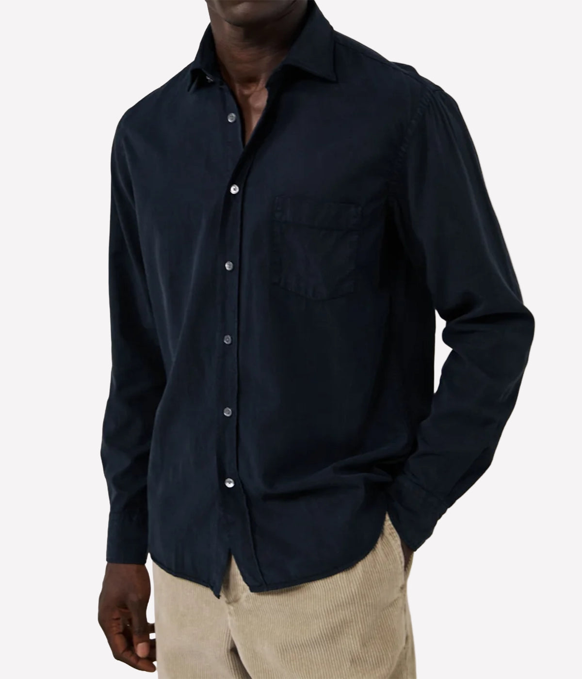 A man wearing a dark navy blue long-sleeve button-down shirt with a chest pocket, paired with beige corduroy trousers, shown against a plain light grey background.