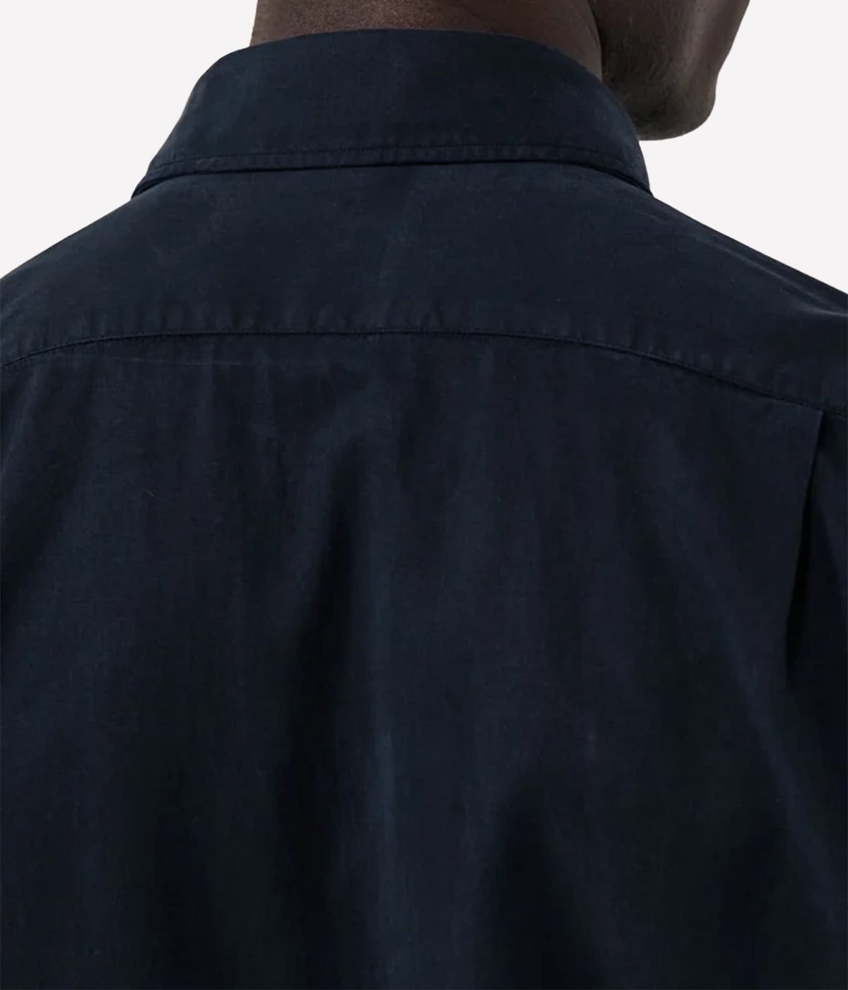 Close-up back view of a person wearing a dark navy button-up shirt, showing the collar and upper back fabric against a plain light background.
