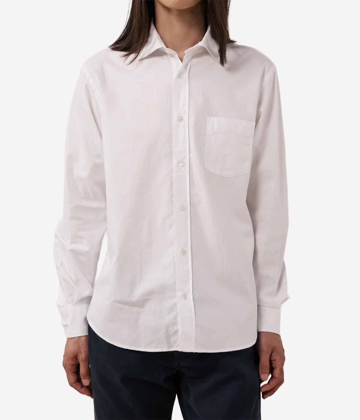 A man wearing a white long-sleeve button-down shirt with a single chest pocket, paired with dark pants.