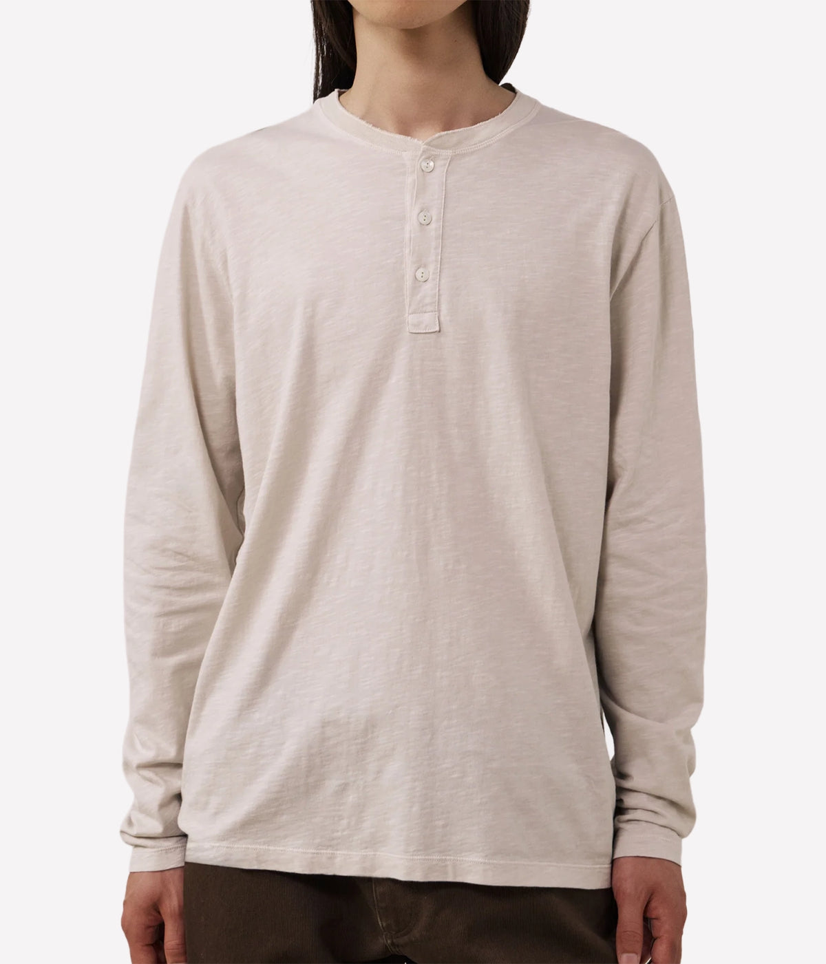 A person wearing a light beige long-sleeve henley shirt with a three-button placket, shown from the neck down against a plain light grey background.