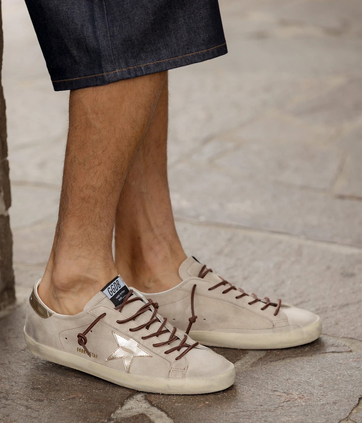 Man wearing Golden Goose Super-Star Sneaker in Beige & Platinum with dark shorts, walking on pavement, side view