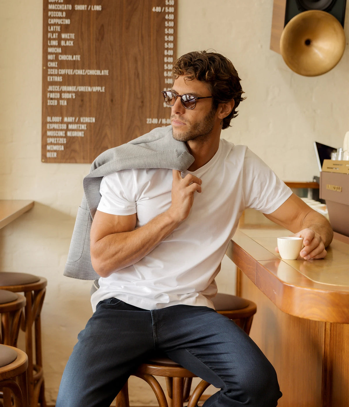 Man seated with Maurizio Baldassari Brera 6pm Herringbone Wool Jacket in Grey draped over his shoulder, worn with a white T-shirt and jeans