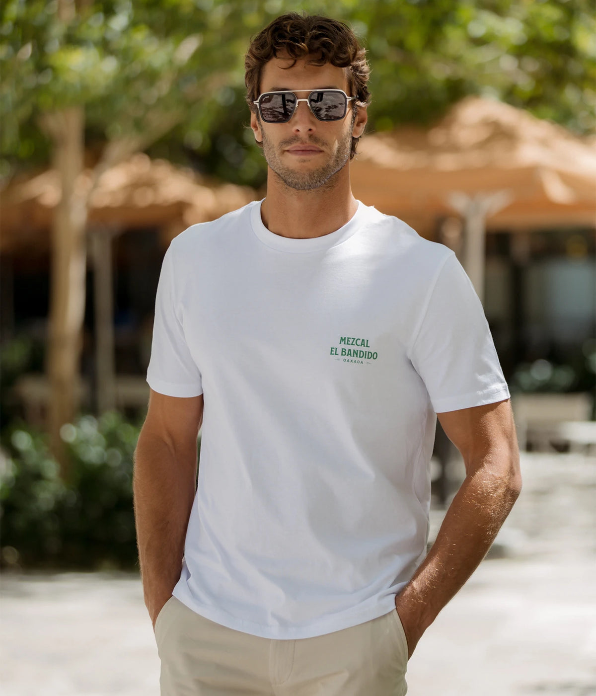Man wearing The Refined Spirit Mezcal Tee in White with beige shorts and sunglasses, standing outdoors, front view