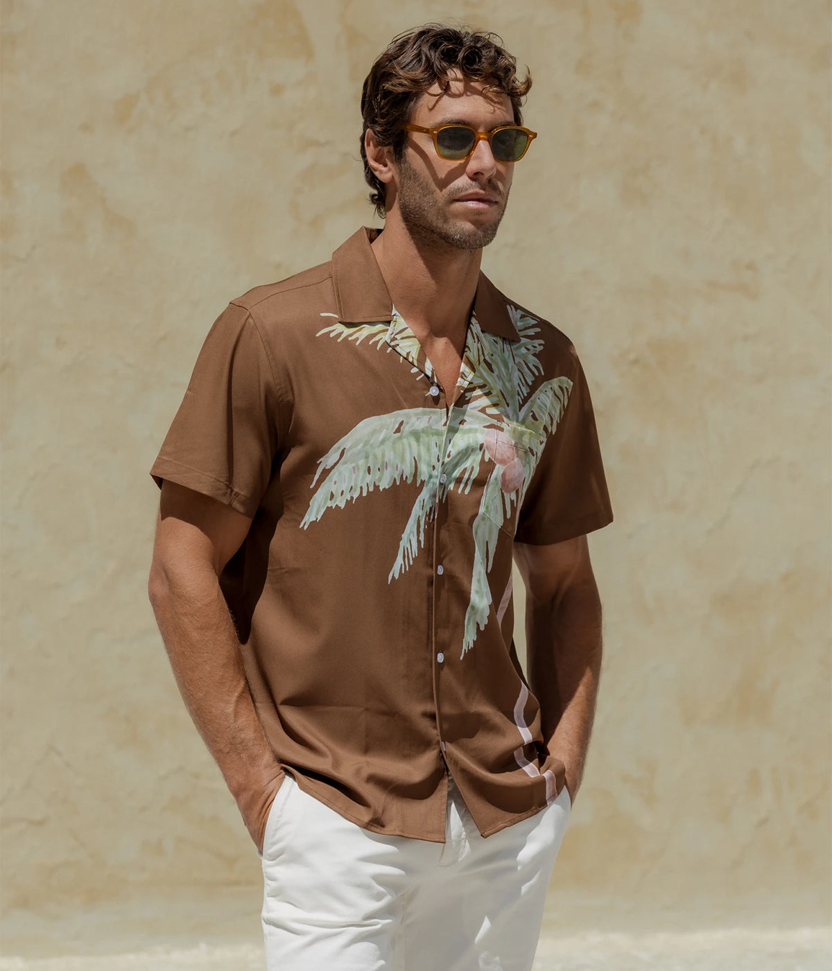 Man wearing Mavrans Coco Weekend Shirt in Brown with white trousers and sunglasses, standing, front view
