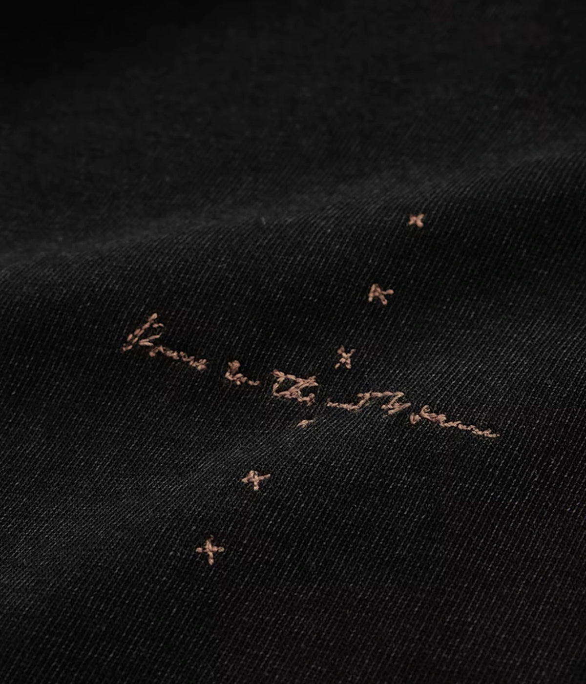 Close-up of John Varvatos Skull Embroidery Raw Edge Tee in Black showing embroidered script and stitch details on the fabric