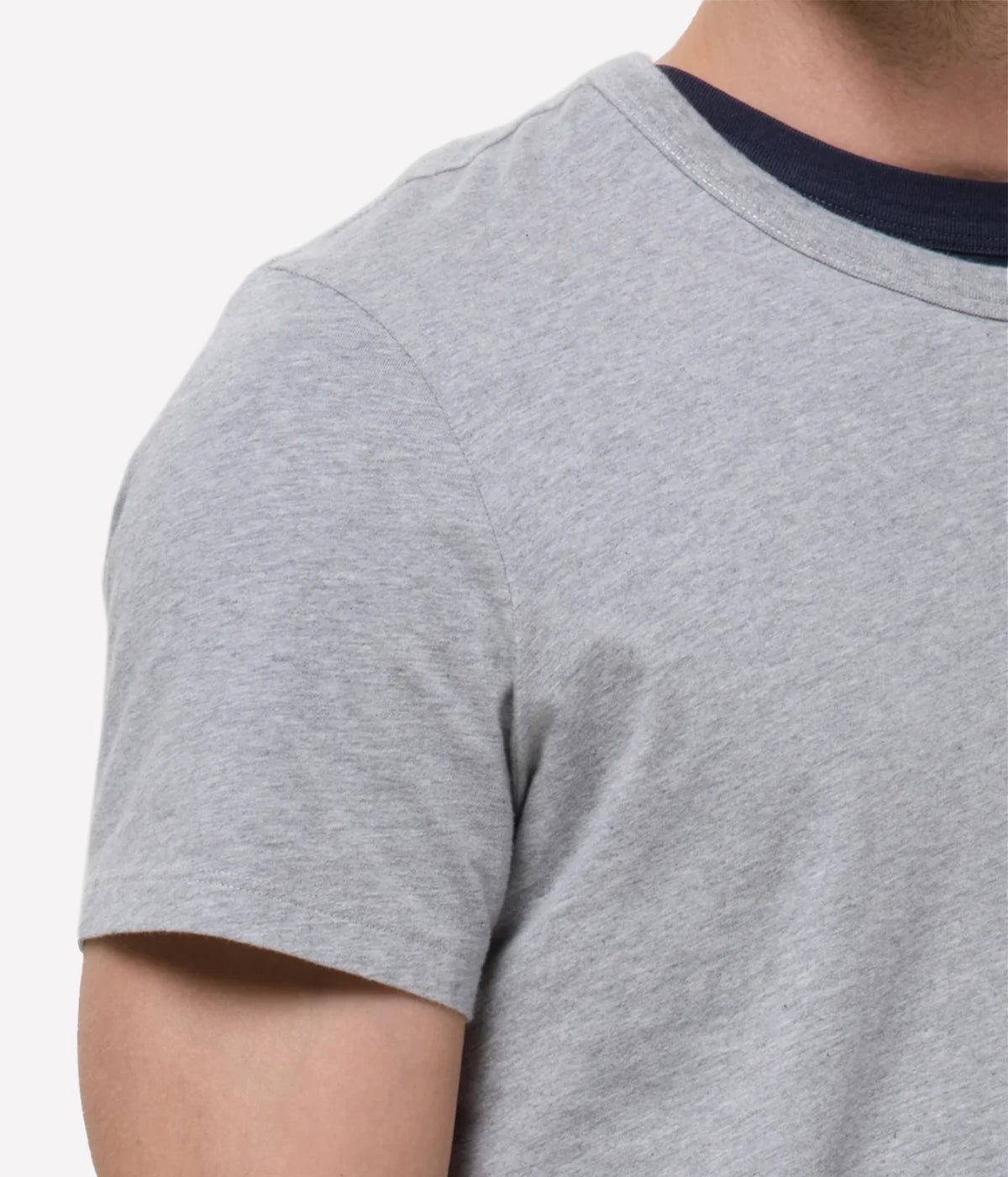Close-up of a person wearing a light heather grey short-sleeve t-shirt with a contrasting dark navy blue crew neck.