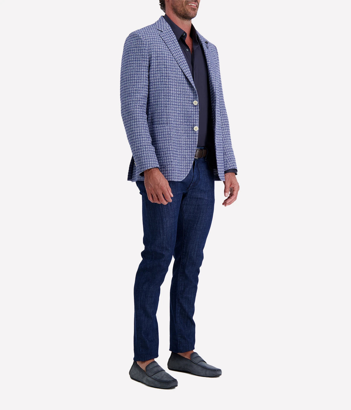 Man wearing a Lardini blue herringbone blazer with a relaxed fit, paired with a cream polo shirt and off-white trousers. The lightweight flax-wool blend fabric drapes effortlessly, featuring a subtle texture and classic herringbone pattern. Styled with sunglasses and an open collar, the look exudes effortless sophistication.