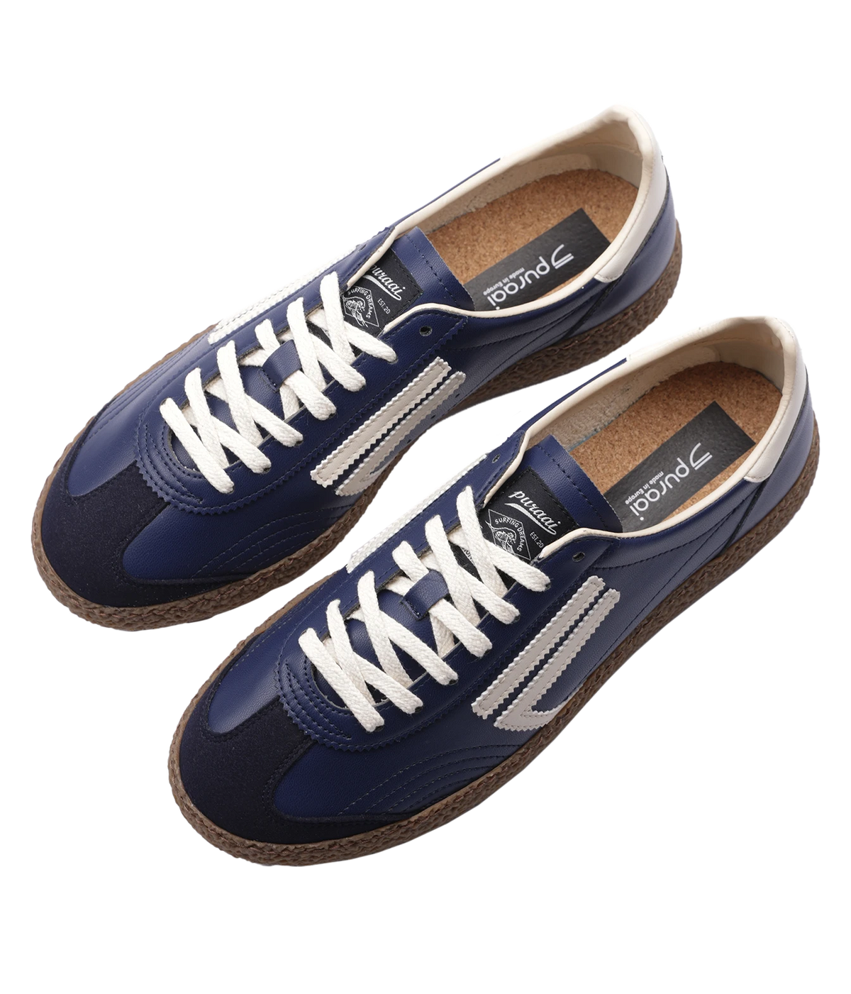 A pair of Puraai sneakers in navy blue, featuring white laces, white side stripes, a brown jute-wrapped sole, and a tan cork-like footbed, shown on a plain white background.