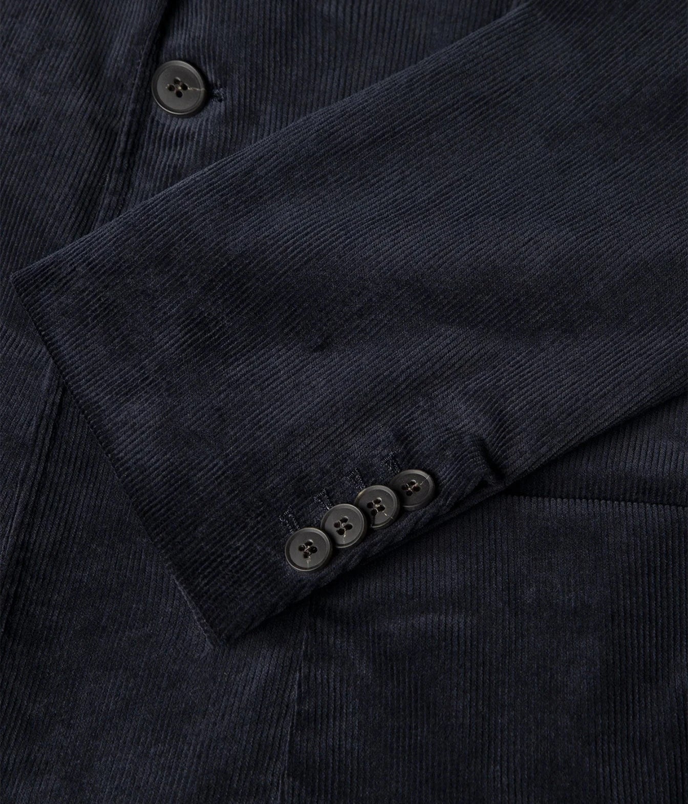 Close-up of a dark navy corduroy jacket or blazer showing the textured fabric, a button placket, and the cuff with four buttons.