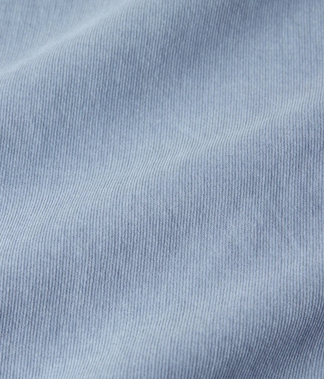 A close-up of light blue ribbed fabric texture with soft folds and a fine knit pattern.