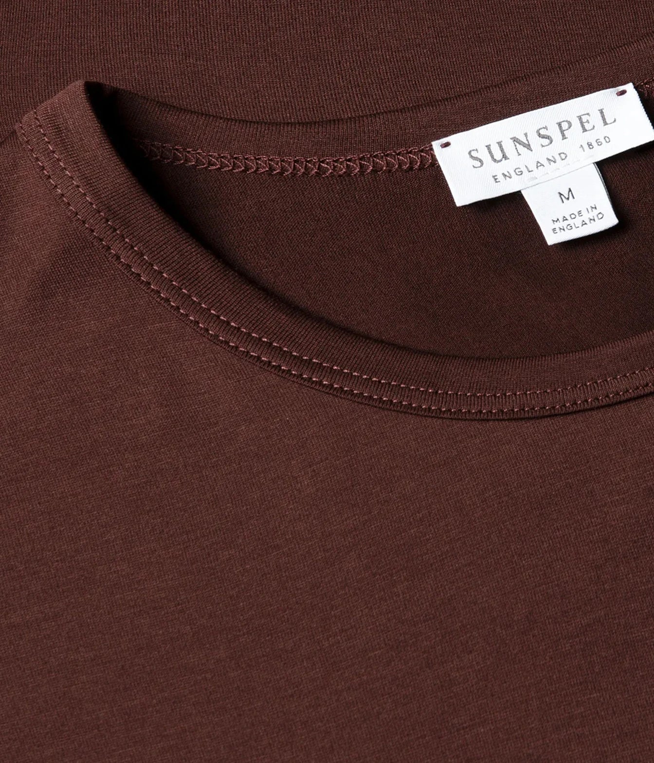 Close-up of a brown crew-neck t-shirt by Sunspel, showing the inner collar with a white brand label.