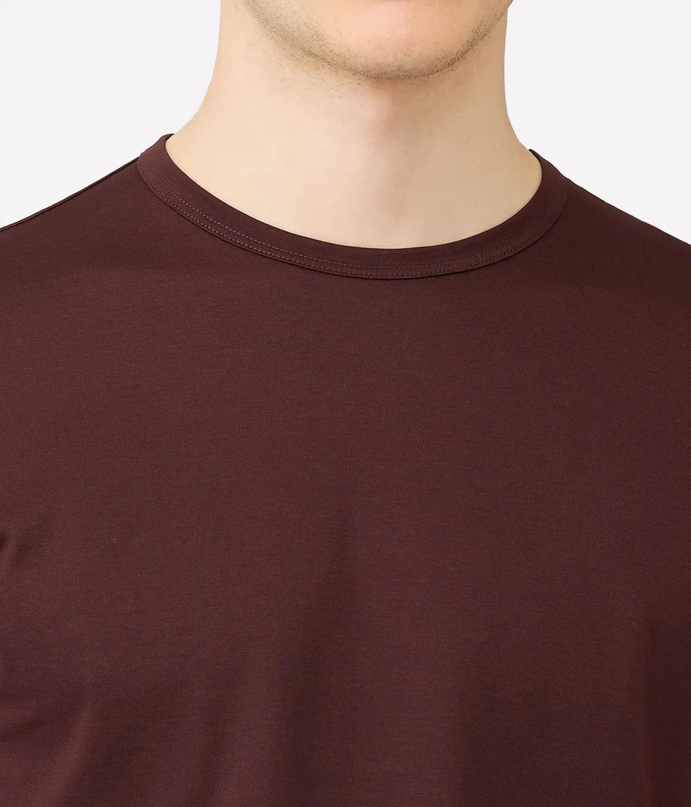 Close-up of a man wearing a solid dark brown crew-neck t-shirt against a light gray background.