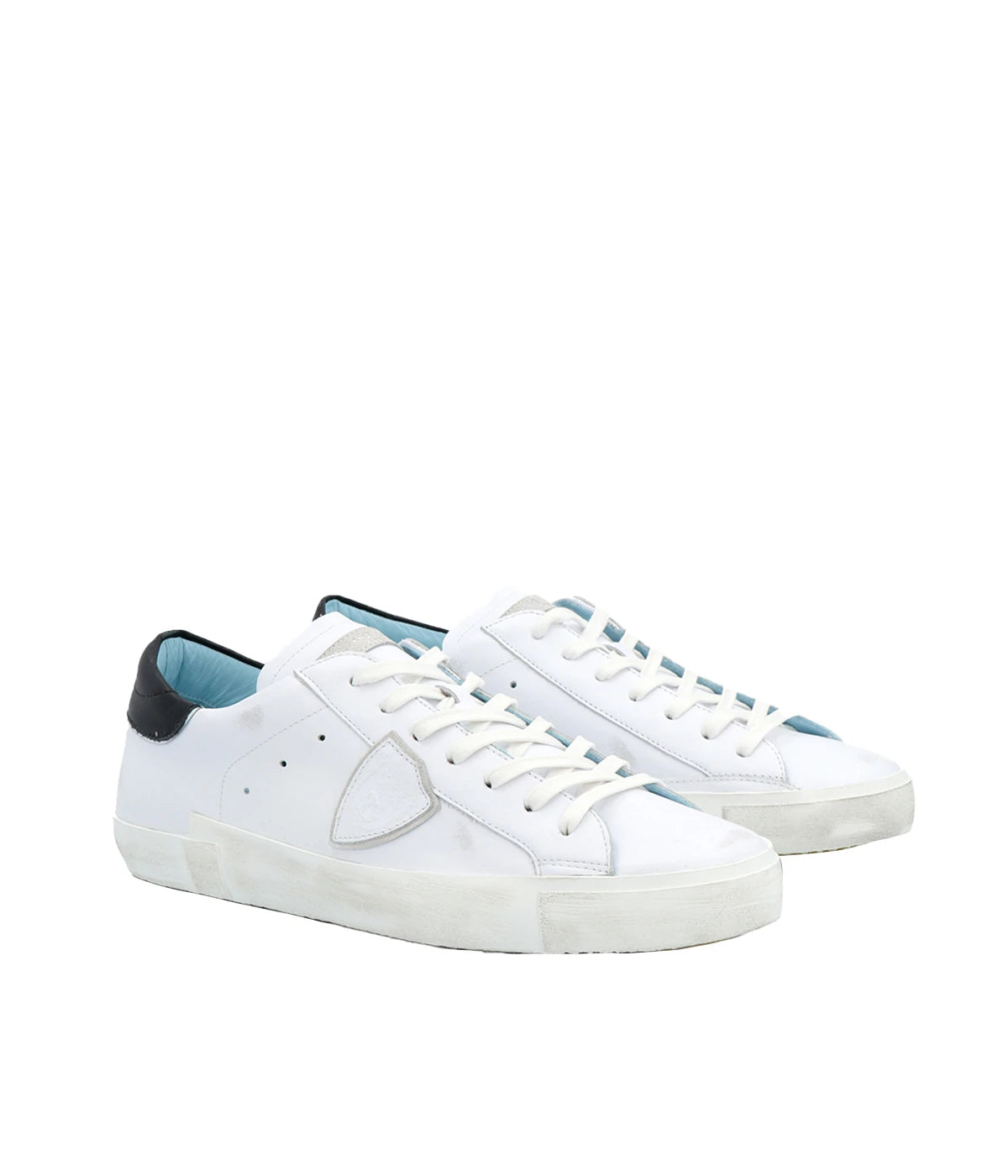 Angle view of Philippe Model PRSX Low Man sneakers, emphasizing the shield on the side of the shoe with the City of Paris coat of arms. The calfskin and suede upper has a worn, vintage-used effect, and the screen-printed laces add to the sneakers' timeless appeal.