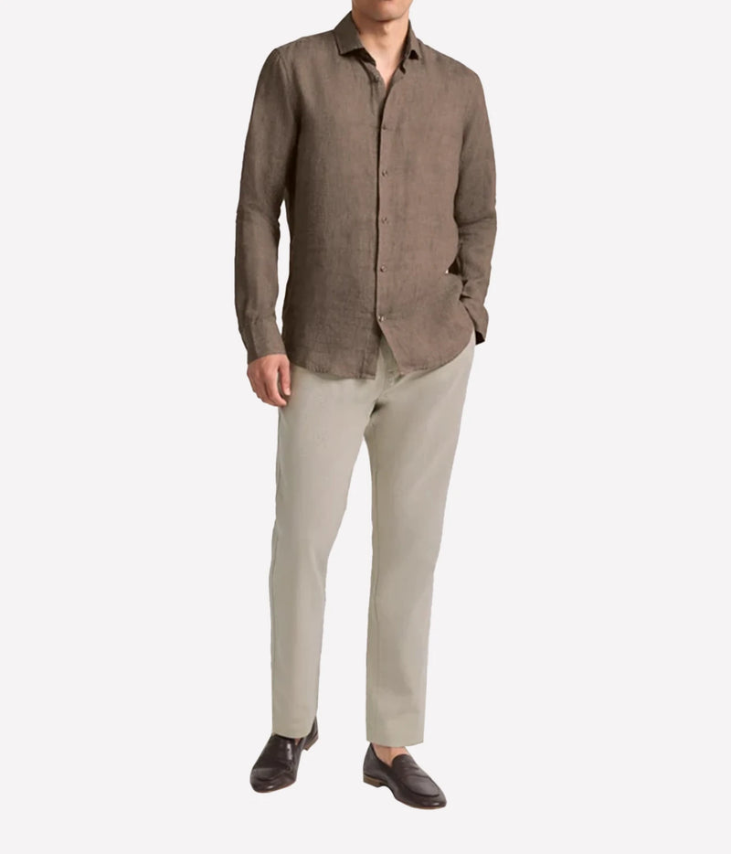 A man wearing a Frescobol Carioca Antonio Linen Long Sleeve Shirt in Dark Mink and light beige trousers, standing against a plain light grey background.