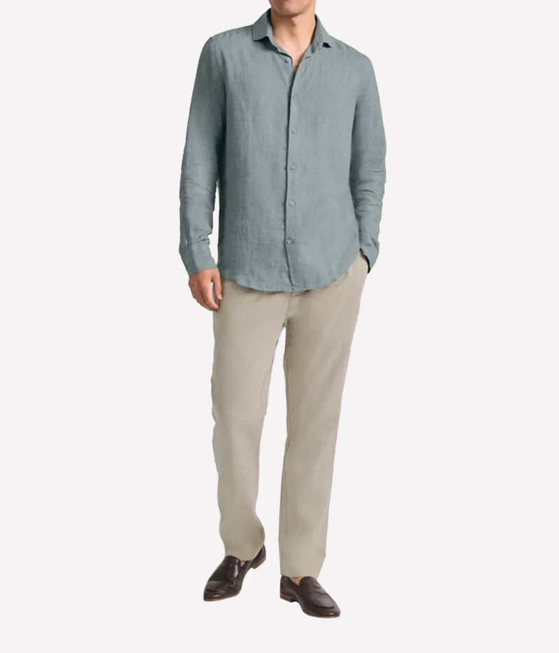 A man wearing Frescobol Carioca Antonio Linen Long Sleeve Shirt in Ash Green, beige trousers, and dark brown loafers, standing against a plain white background.