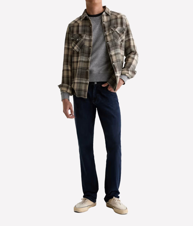 Man wearing AG Graduate Jean in Studio with a check overshirt, charcoal tee and cream sneakers, front view