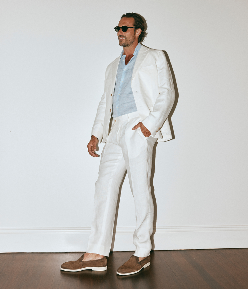 Man wearing a white suit with sunglasses against a plain background