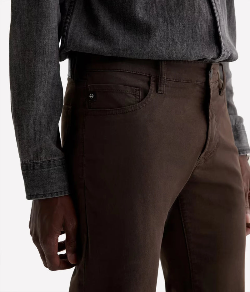 Close-up of a person wearing dark brown slim-fit jeans with a dark gray denim shirt tucked in, shown from the waist down against a plain white background.