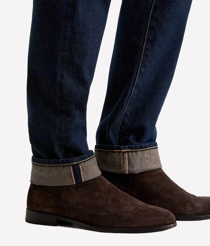 Close-up of AG Tellis Selvage Jean in 3 Years Out Of The Blue showing the cuffed selvage hem with brown suede boots