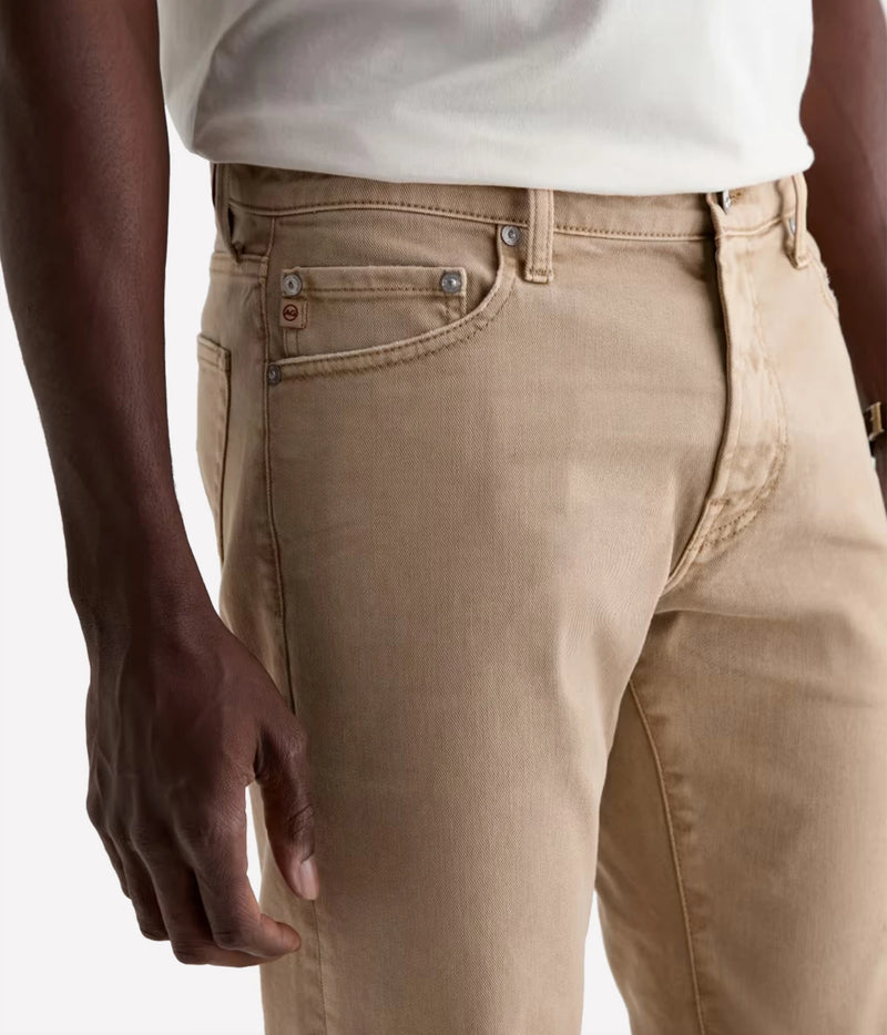 Close-up of a person wearing beige denim jeans with a white t-shirt, showing the front pocket and waistband details.