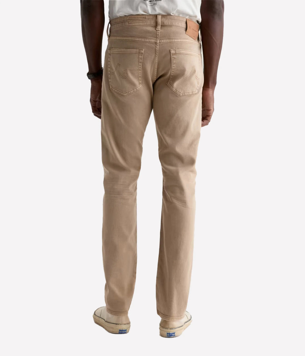A person shown from the back wearing beige straight-leg jeans, a white t-shirt, and beige sneakers against a light gray studio background.