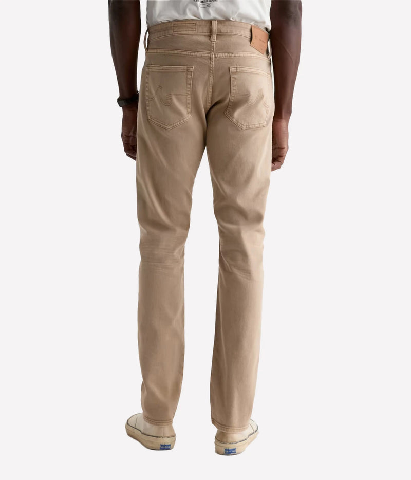 A person shown from the back wearing beige straight-leg jeans, a white t-shirt, and beige sneakers against a light gray studio background.