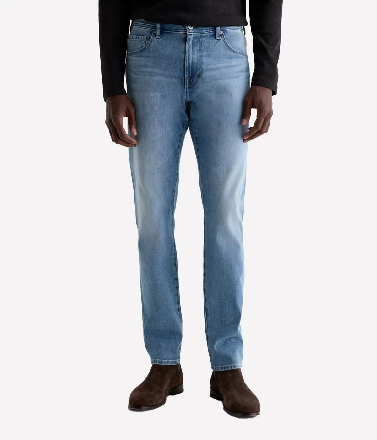 A person wearing light blue slim-fit jeans, a black long-sleeve top, and brown suede boots, shown from the waist down against a light gray studio background.