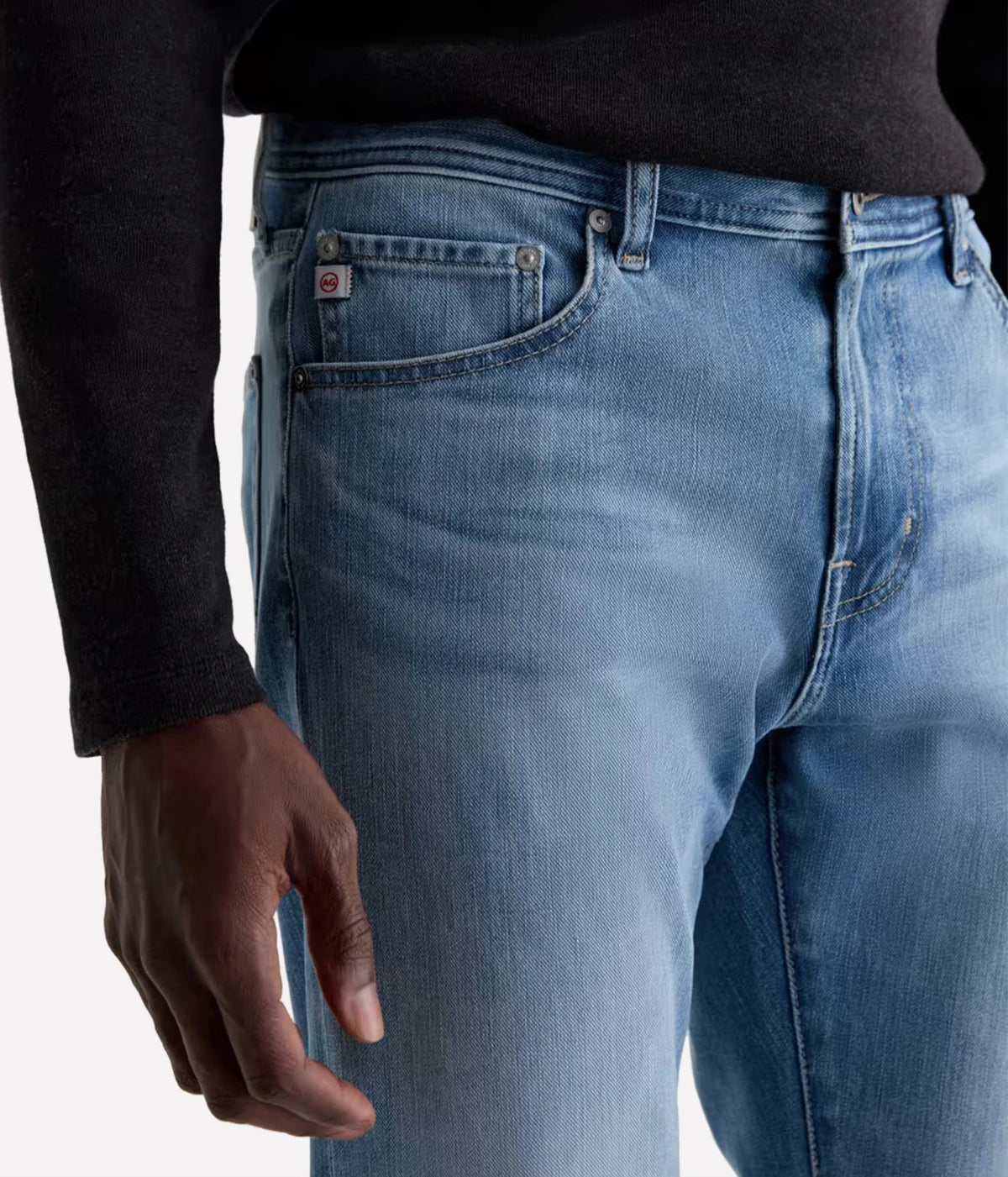 Close-up of a person wearing light blue denim jeans with a black long-sleeve top, showing the back pocket and waistband area against a plain light background.