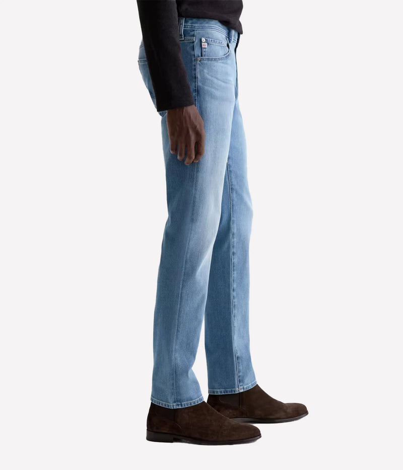 A side profile view of a person wearing light blue straight-leg denim jeans, a black long-sleeve top, and dark brown suede boots against a plain white background.